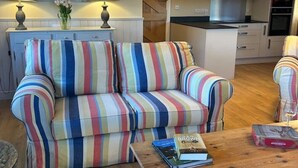 A living room with a striped sofa, a wooden coffee table, and a kitchen in the background. - A family and dog friendly haven, The Hayloft. (Sweffling)