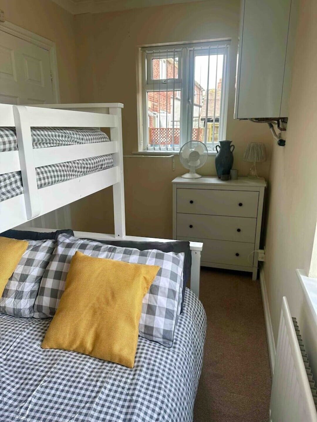 A bedroom with a bunk bed, a bedside table with a lamp, and a window with a view of buildings.