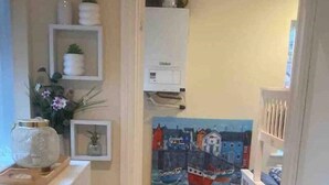 Un pasillo estrecho con una puerta blanca que da a una habitación con suelo de baldosas y un cuadro de barcos.