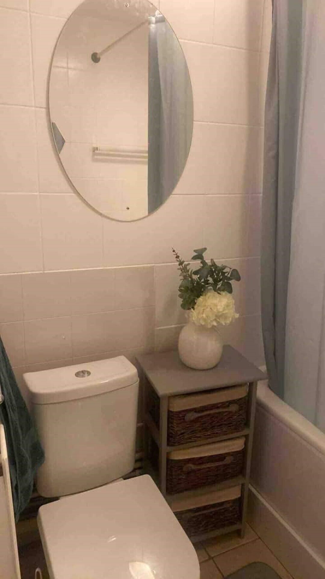 A bathroom with a toilet, a sink, a mirror, and a small cabinet with a vase of flowers.