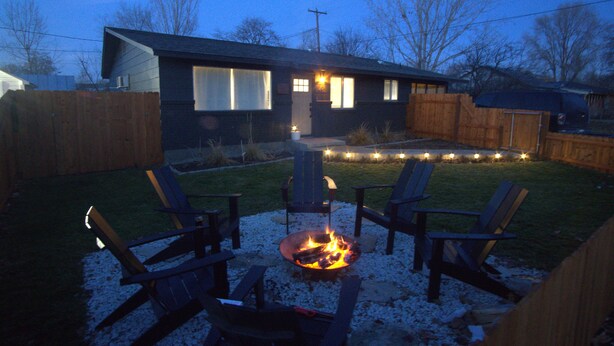 Un patio trasero con un hogar, dos sillas Adirondack y una casa con una terraza.