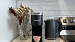 Una cafetera Keurig con jarra y un florero de cristal con flores secas sobre una encimera de cocina.
