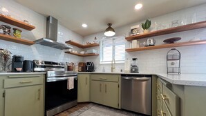 Una cocina moderna con armarios verde claro, electrodomésticos de acero inoxidable, repisas de madera y una isla central.