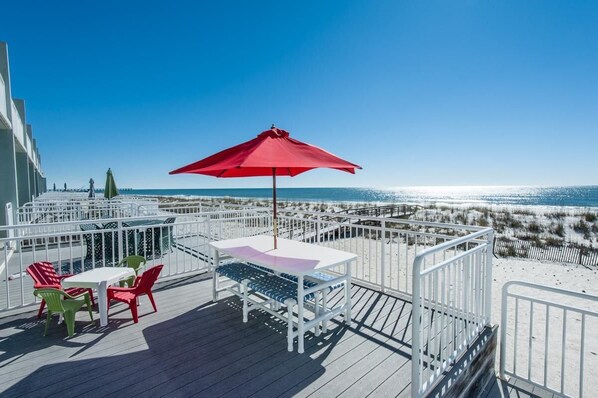 A deck with a table and chairs, a red umbrella, and a view of the beach and ocean.