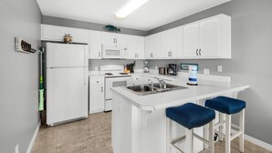 Une cuisine moderne avec des meubles blancs, un îlot central doté de tabourets, un réfrigérateur et un four à micro-ondes.