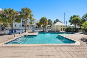 A swimming pool with a tiled deck, a small gazebo, and palm trees.