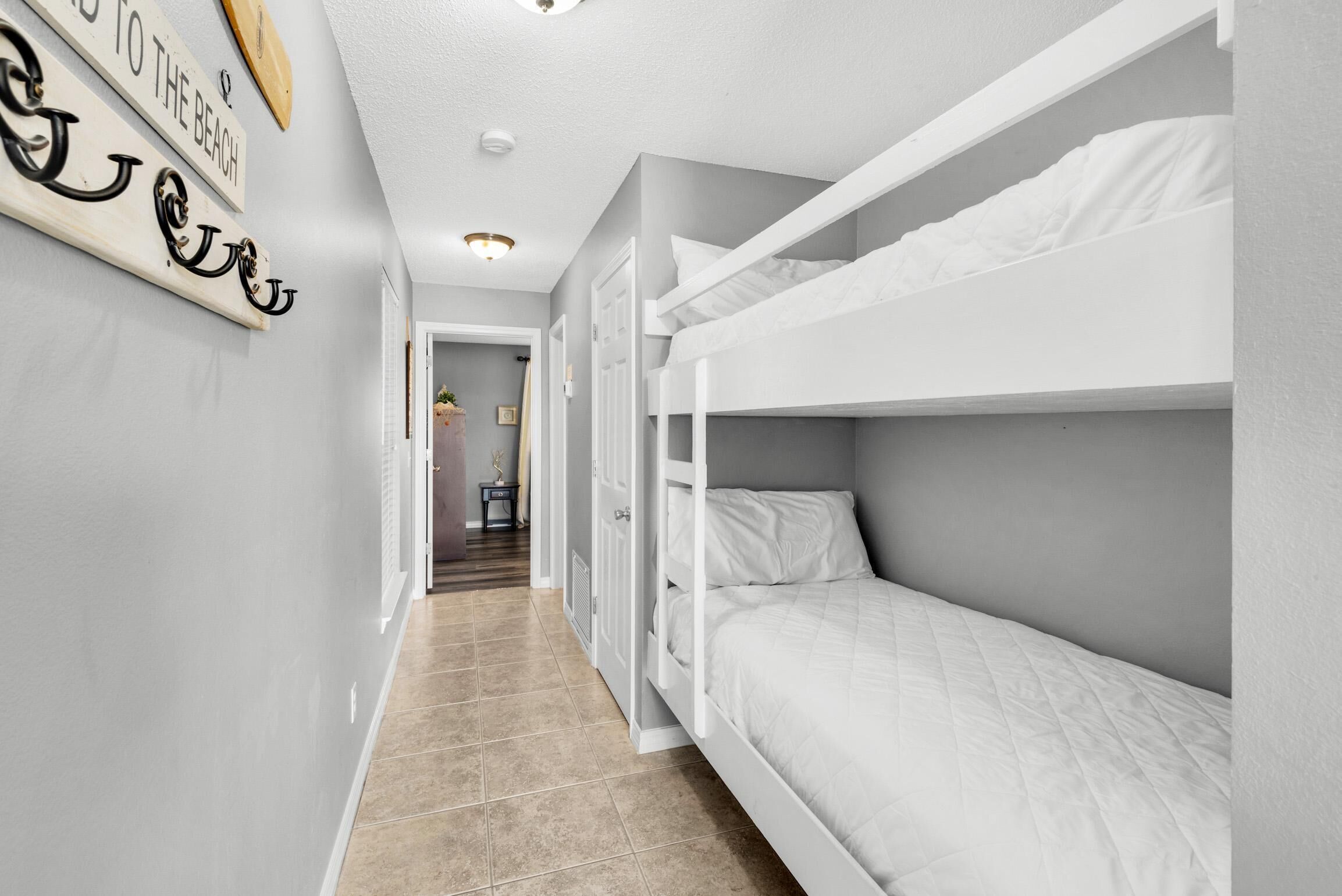 A narrow hallway with a bunk bed on the right, a door at the end, and a wall with decorative items.
