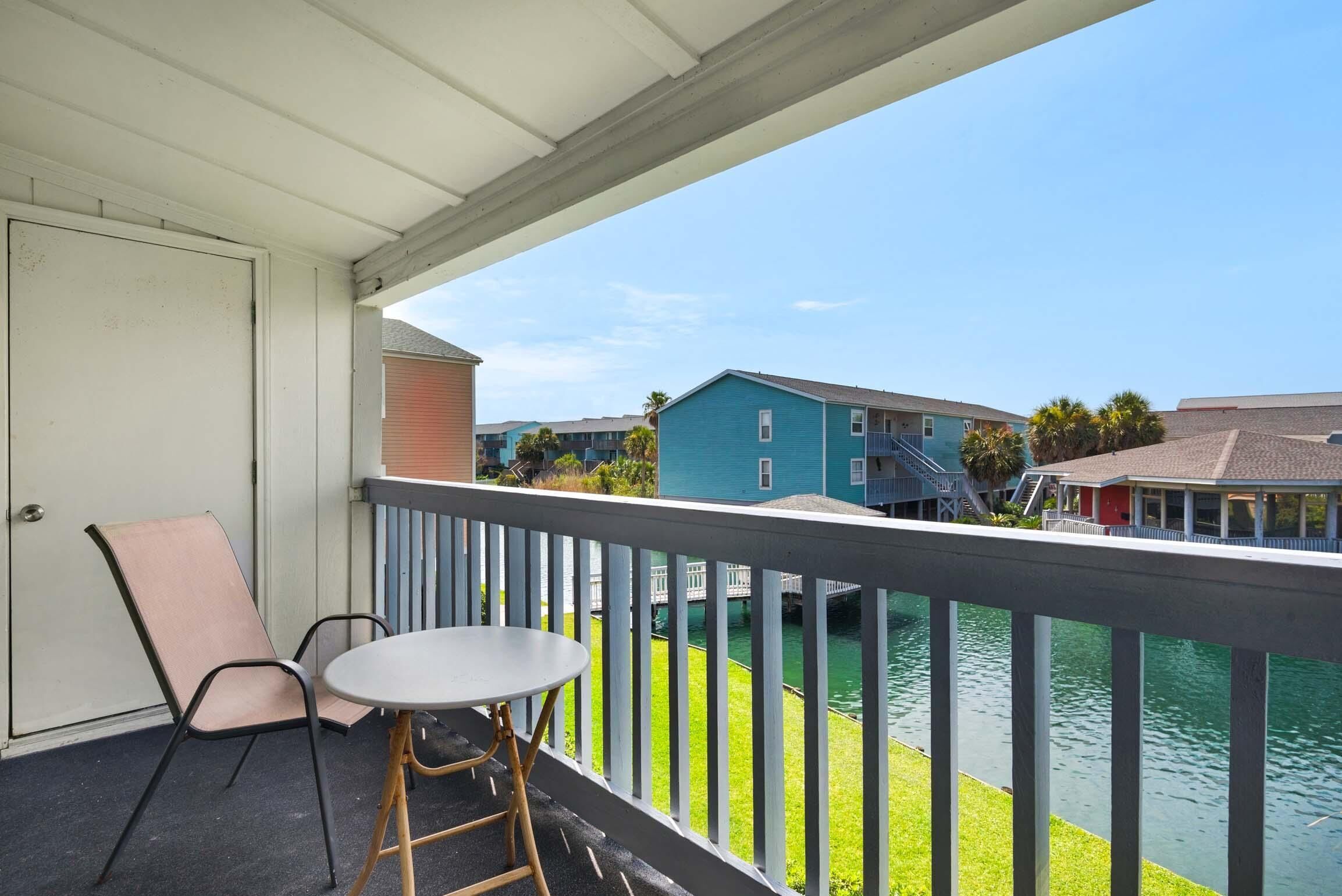 A balcony with a table and chairs, overlooking a body of water and neighboring buildings.