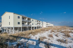A beachfront hotel with multiple floors, balconies, and a pier extending into the water. - Villas on the Gulf Unit E4 (Pensacola Beach)
