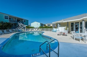 A swimming pool with a 5 ft depth marker, surrounded by lounge chairs and a building with a balcony. - Villas on the Gulf Unit E4 (Pensacola Beach)