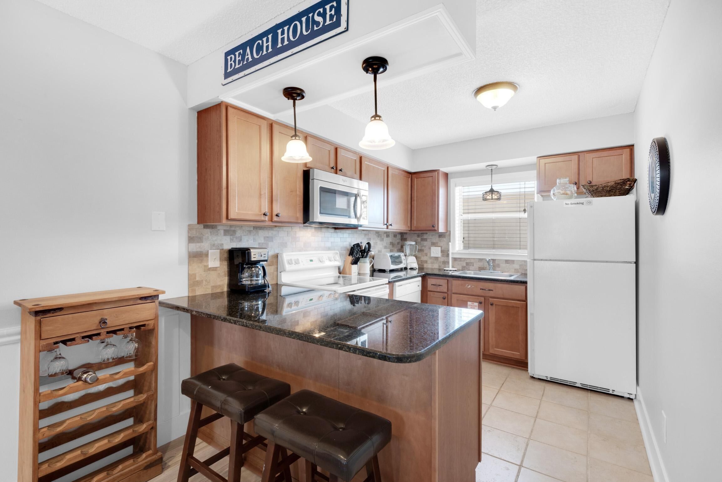 A kitchen with wooden cabinets, a central island with stools, a microwave, stove, and a refrigerator.