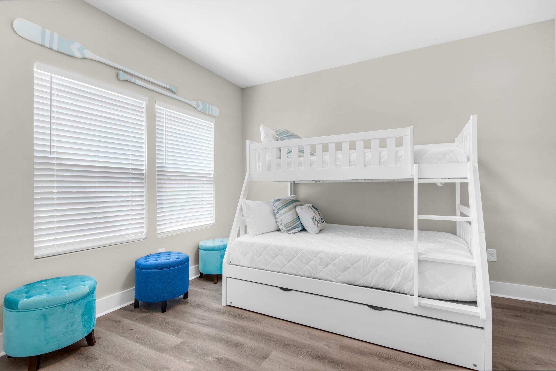 A bunk bed with a ladder, two ottomans, and a window with blinds.
