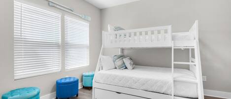A bunk bed with a ladder, two ottomans, and a window with blinds.