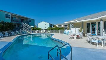A swimming pool with a 5 ft depth marker, surrounded by lounge chairs and a building with a balcony.