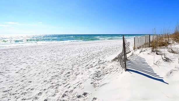 A sandy beach with a wooden fence and sparse vegetation. - Villas on the Gulf Unit G8 (Pensacola Beach)