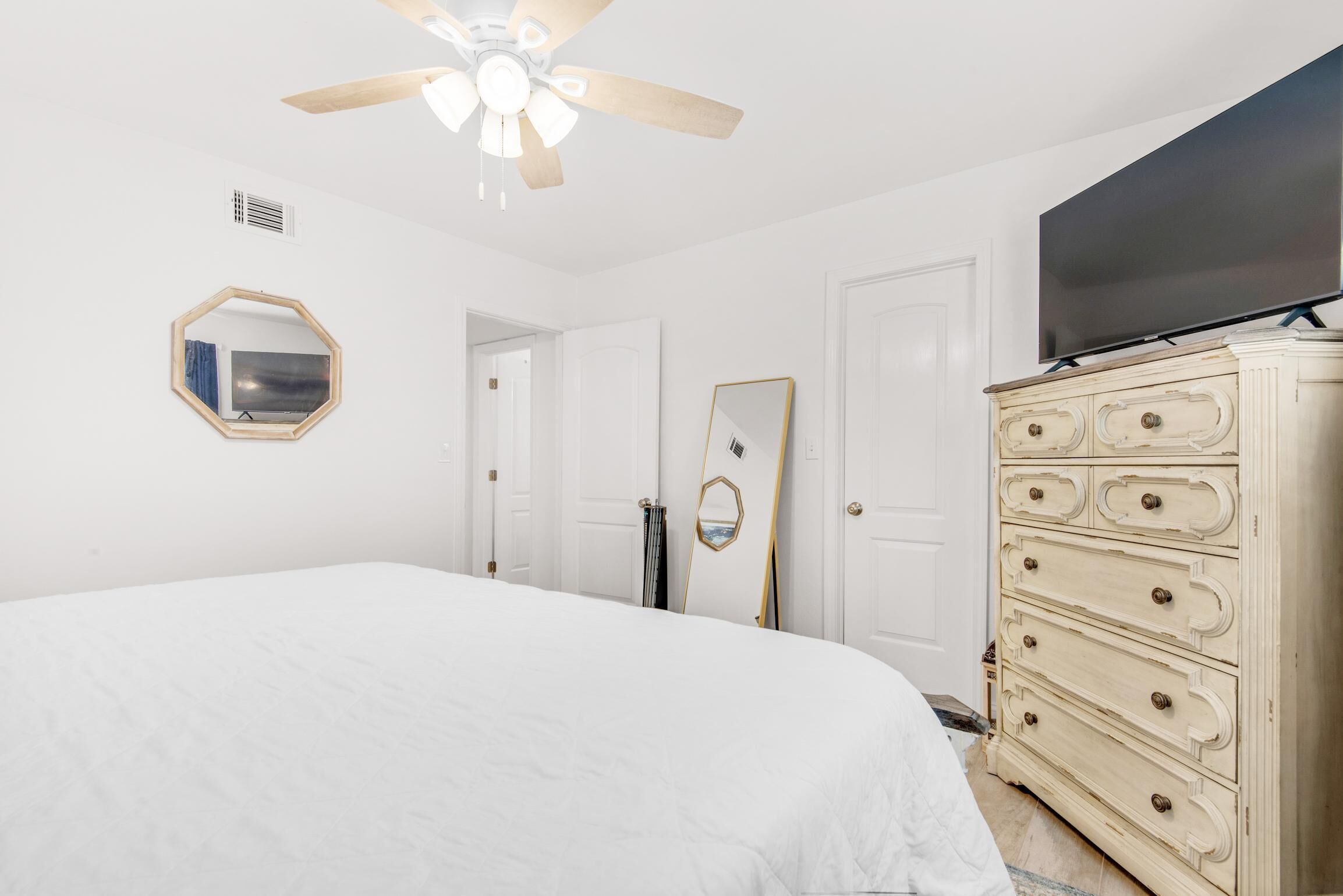 A bedroom with a bed, a dresser, a ceiling fan, a TV, and a mirror.