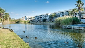 A waterfront hotel with a pool, palm trees, and a dock. - Villas on the Gulf Unit G8 (Pensacola Beach)