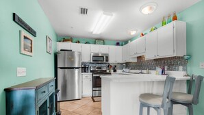A kitchen with white cabinets, a stainless steel refrigerator, a microwave, and a sink. - Sunset Harbor Villas 313 (Navarre)