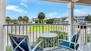 A balcony with a table and chairs, overlooking a street with palm trees and buildings. - Sunset Harbor Villas 313 (Navarre)