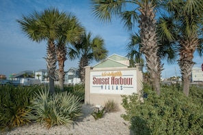 A sign for Sunset Harbour Villas with a clear view of the surrounding palm trees and a building in the background. - Sunset Harbor Villas 313 (Navarre)