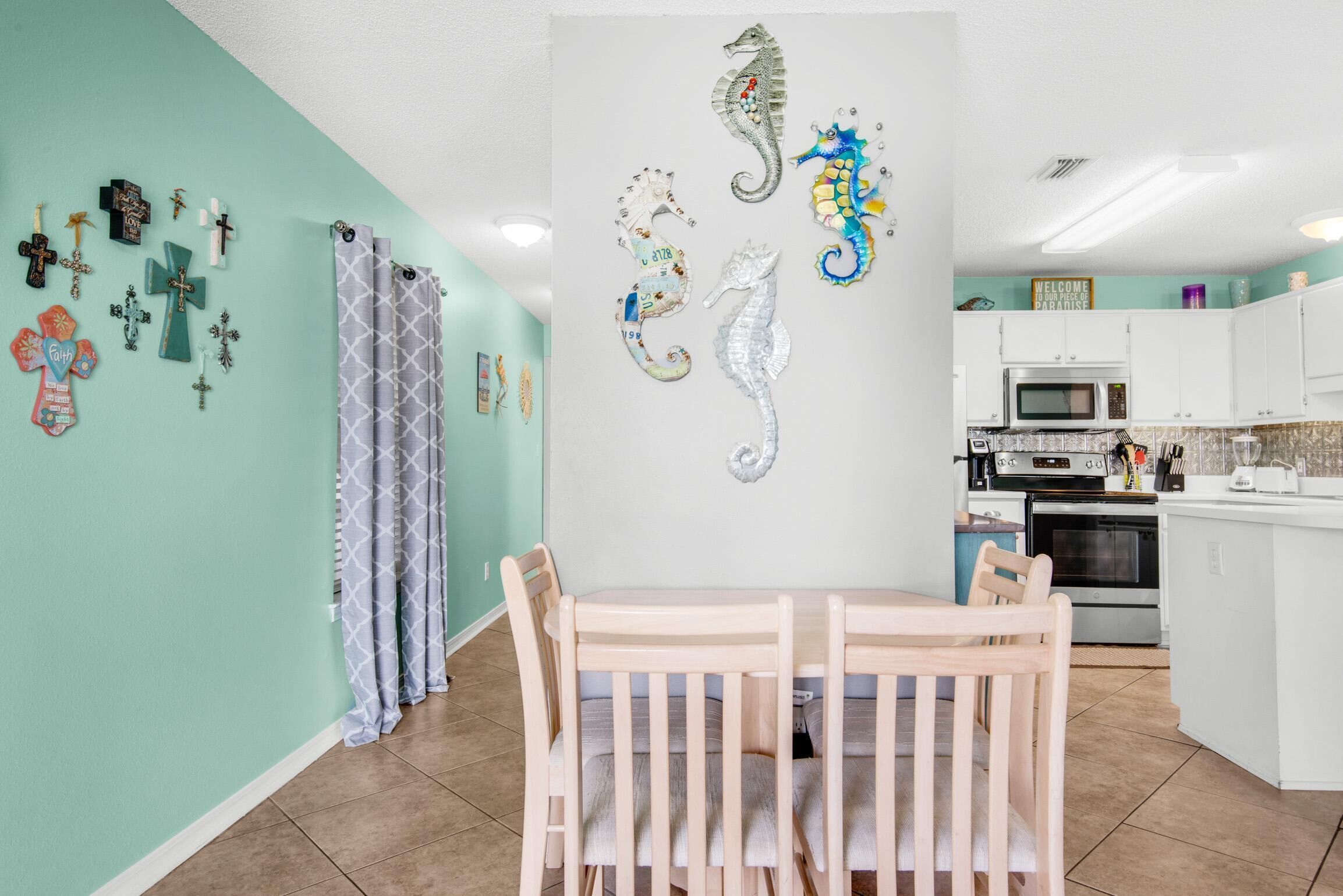 Une cuisine avec un coin repas, des murs de couleur turquoise et des décorations murales représentant des hippocampes.