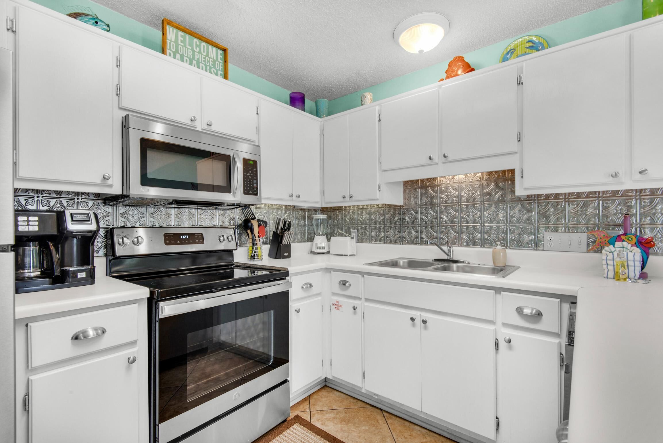 A kitchen with white cabinets, a microwave, a stove, a sink, and a tiled backsplash.
