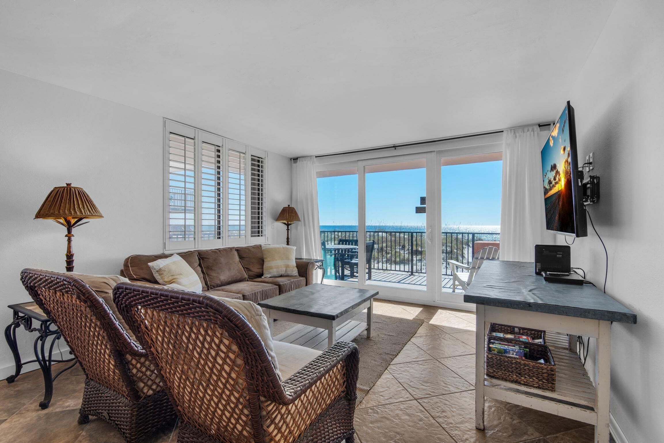 A living room with a sofa, wicker chairs, a coffee table, a TV, and a balcony with a view.