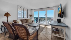 Ein Wohnzimmer mit einer Couch, Korbstühlen, einem Couchtisch, einem Fernseher und einem Balkon mit Blick.