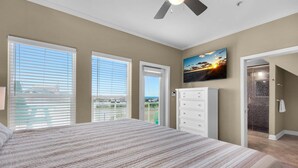 A bedroom with a large bed, a ceiling fan, a TV, and a view of the outside.