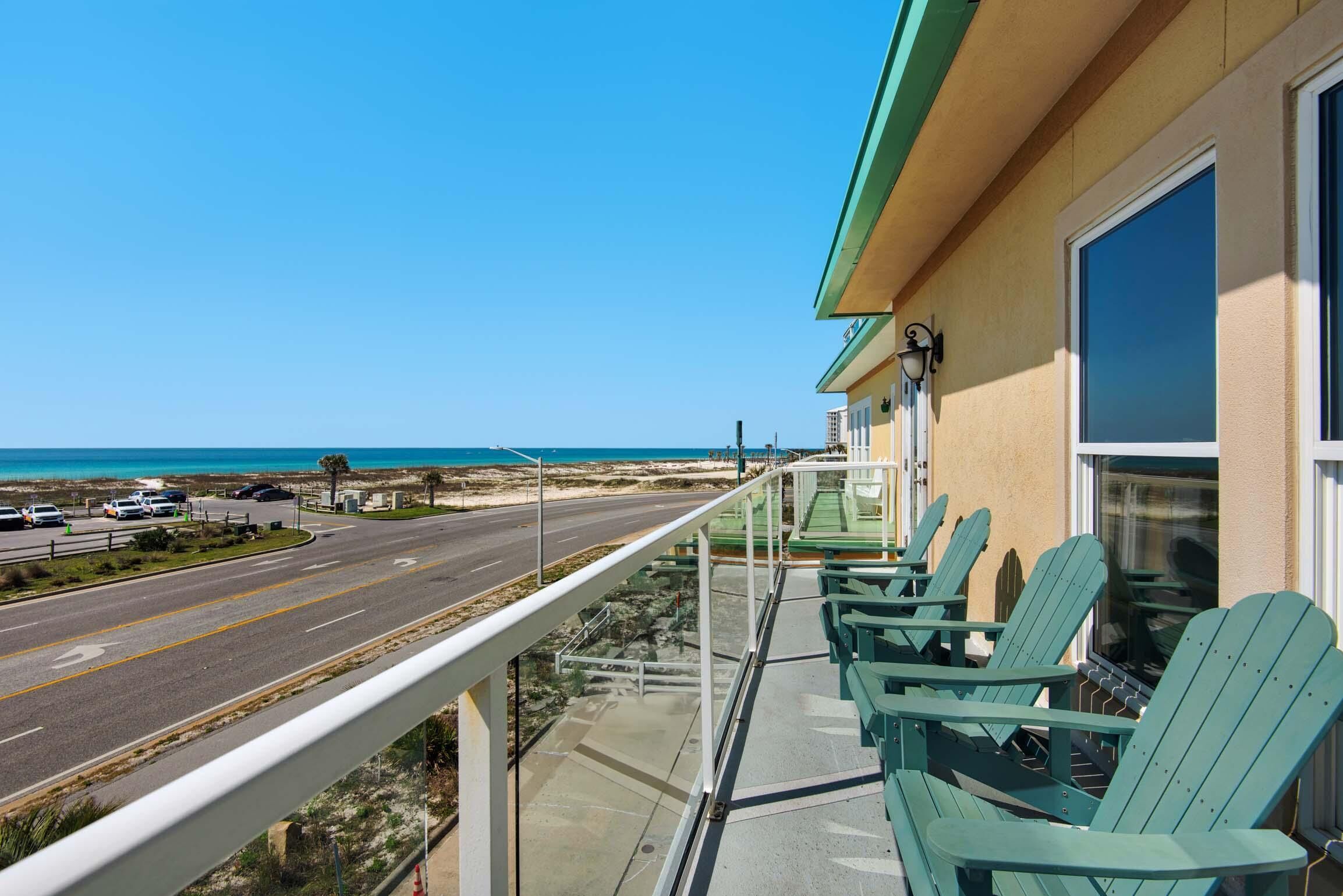 A balcony with green Adirondack chairs overlooking a beach and a road.