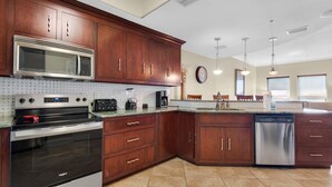 A kitchen with wooden cabinets, a stainless steel microwave, a built-in oven, a dishwasher, and a tiled backsplash.