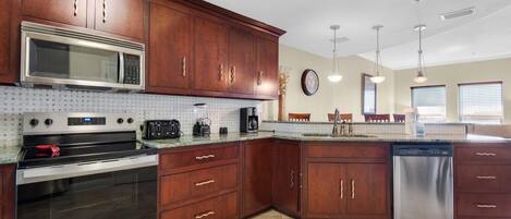 A kitchen with wooden cabinets, a stainless steel microwave, a built-in oven, a dishwasher, and a tiled backsplash.