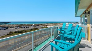 A balcony with turquoise chairs overlooking a parking lot and a beach.