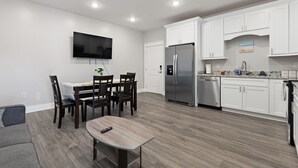 A modern kitchen with white cabinets, a stainless steel refrigerator, and a dining area with a table and chairs. - Fun in the Sun 2 Bed Apt. (Biloxi)