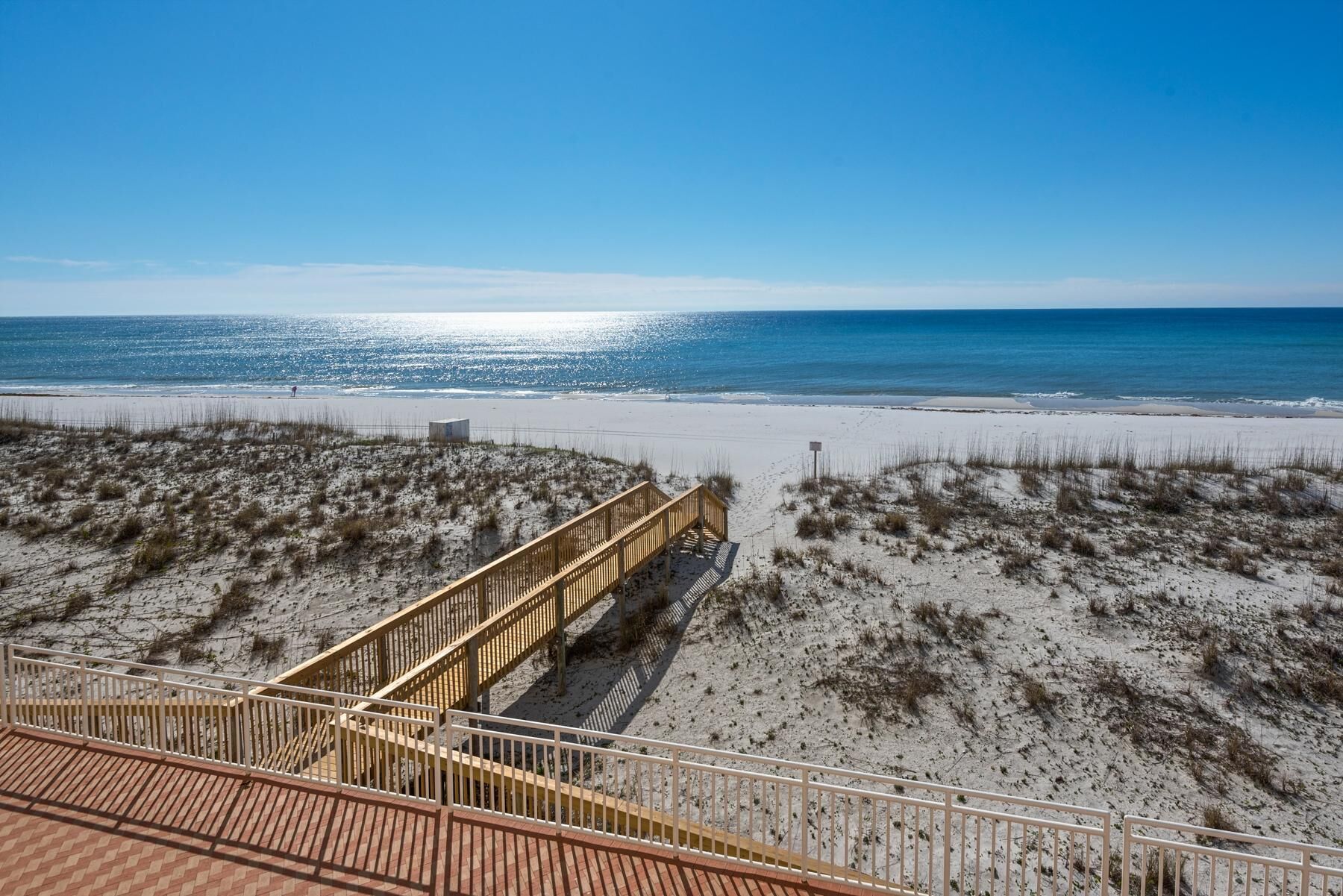 Vista de la playa con un paseo marítimo de madera que conduce a una zona arenosa.