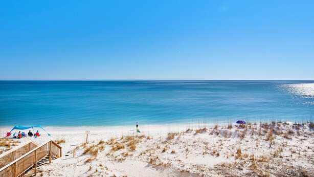 A beach with a wooden boardwalk, a tent, and a lifeguard tower. - Sans Souci Unit 209 (Pensacola Beach)