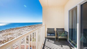 A balcony with two wicker chairs, a view of the beach, and a clear sky. - Sans Souci Unit 209 (Pensacola Beach)