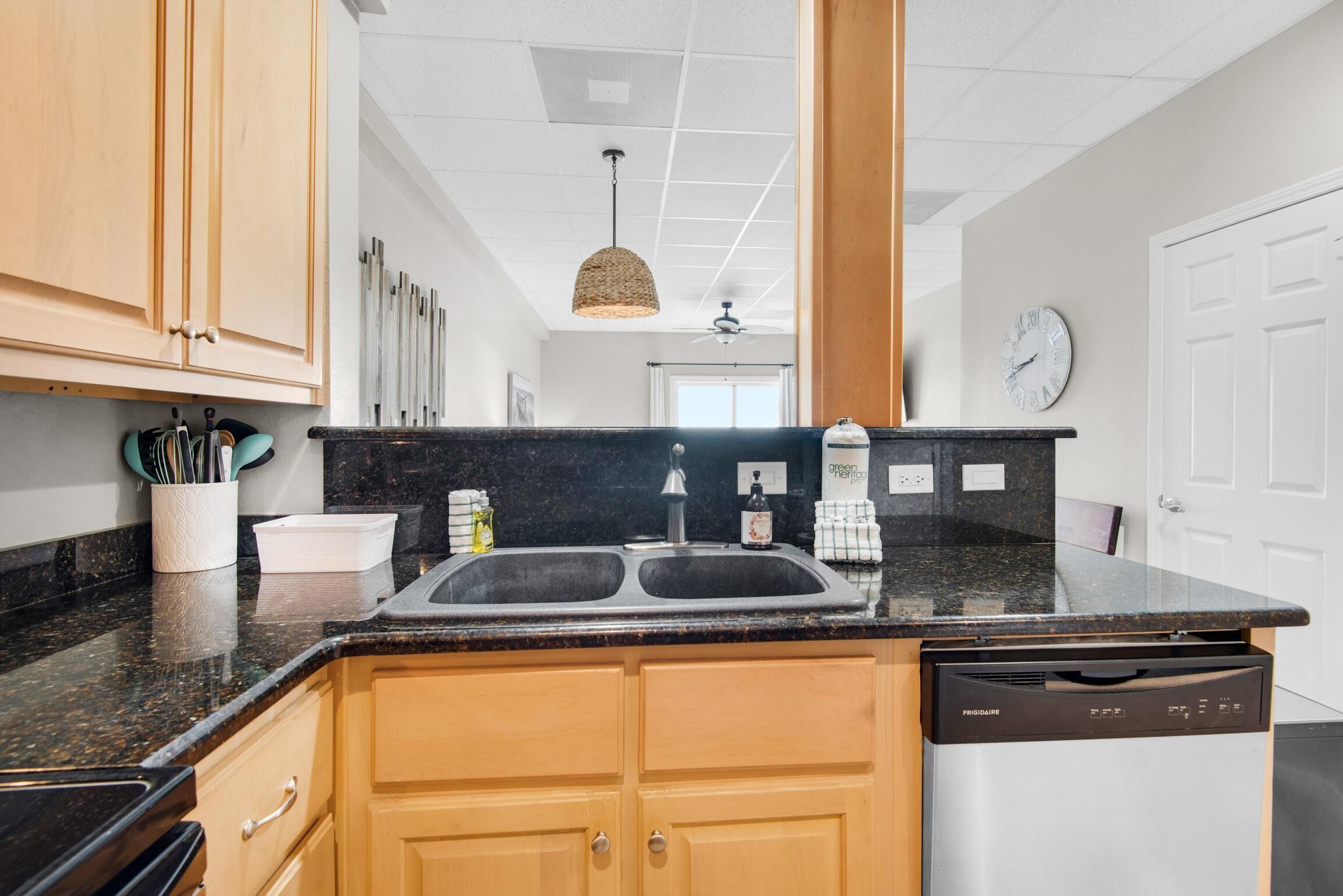 A kitchen with wooden cabinets, a black granite countertop, a double sink, and a dishwasher.