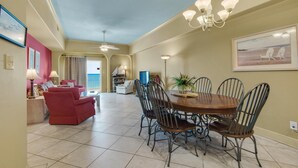 A dining area with a round table and chairs, a chandelier, and a view of the ocean through a door. - Sans Souci Unit 704 (Pensacola Beach)