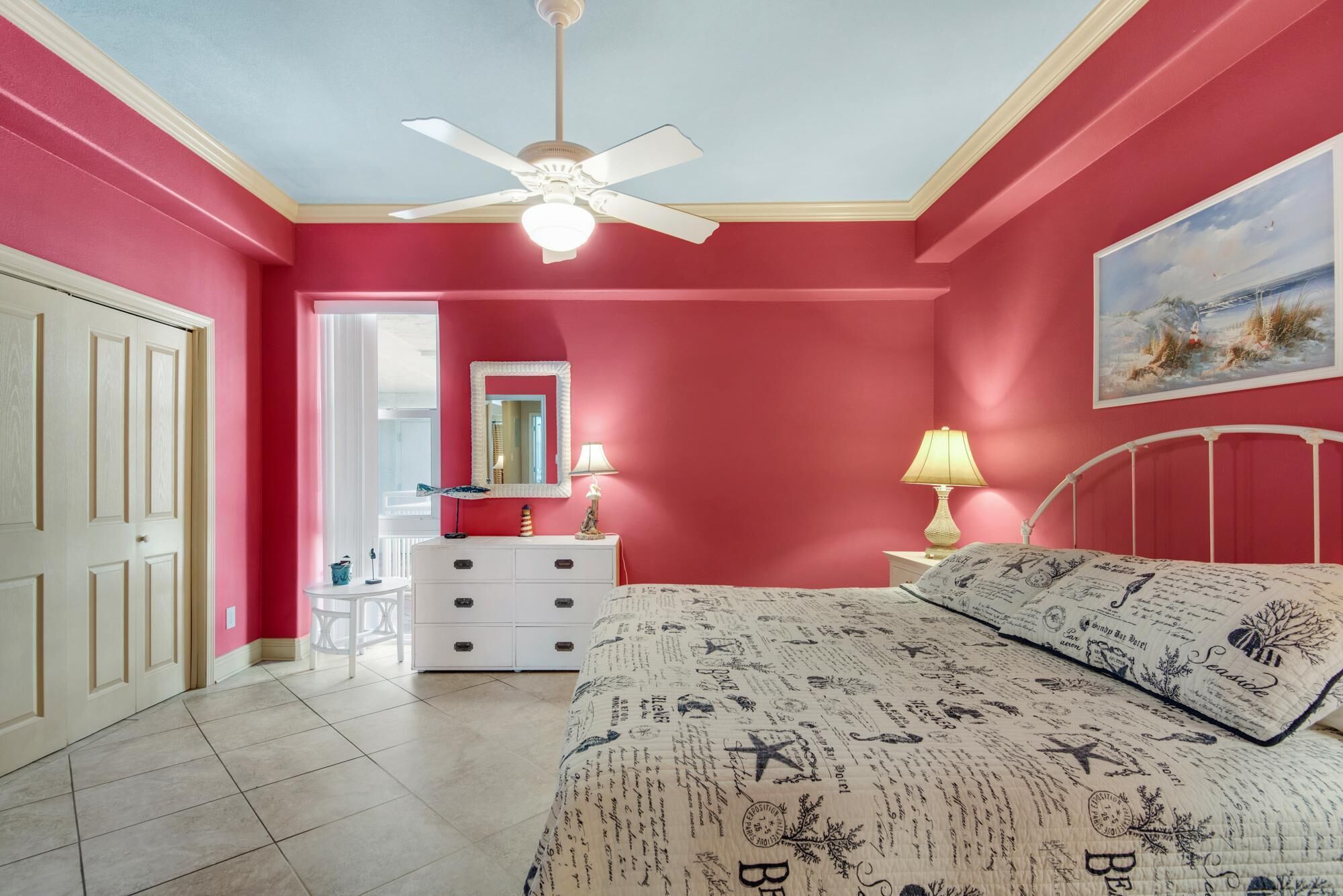 Un dormitorio con cama, mesita de noche, cómoda, ventilador de techo y un cuadro en la pared.