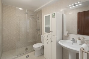 Un baño moderno con ducha de vidrio, inodoro y lavamanos con espejo.