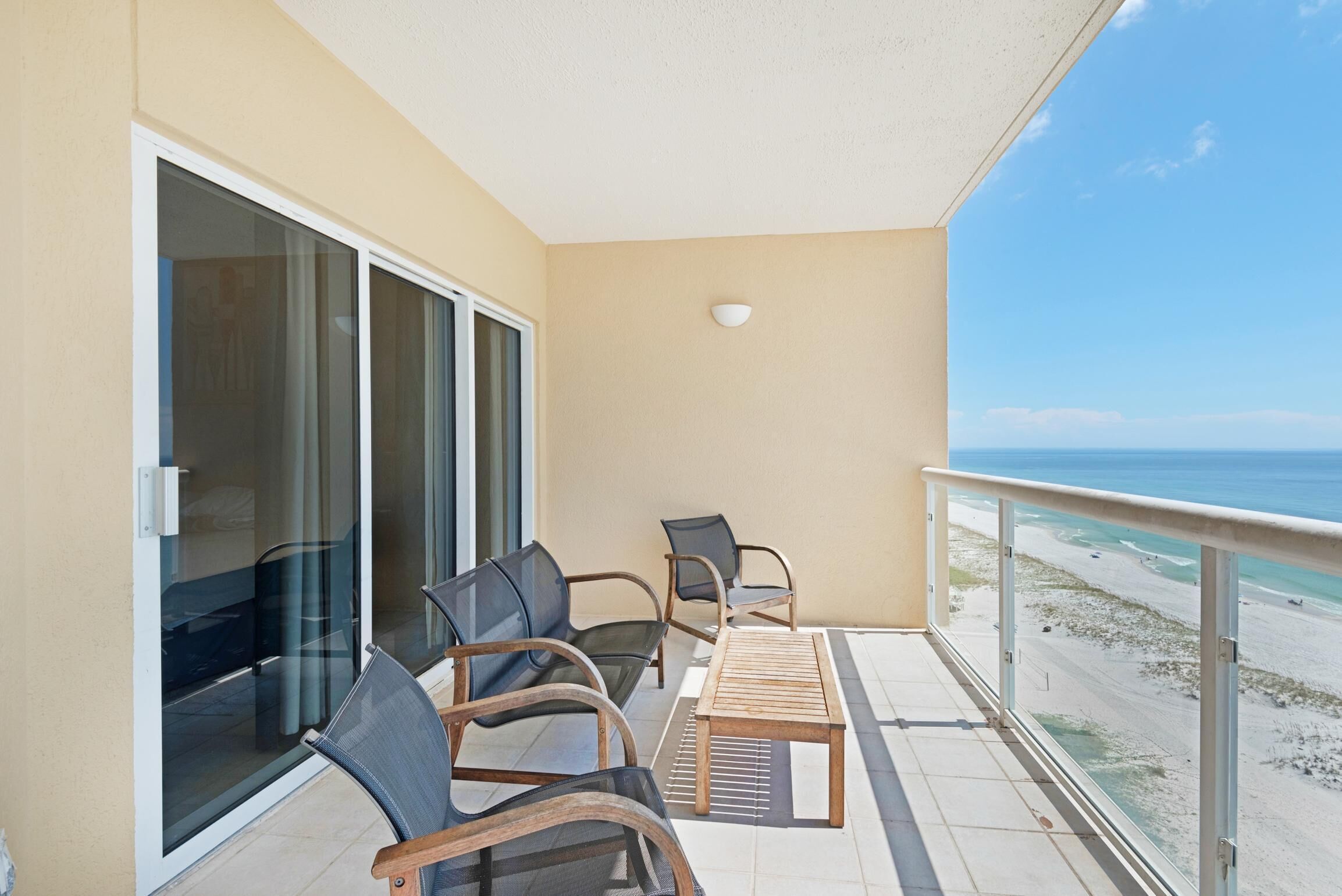 A balcony with a table and chairs, a sliding glass door, and a view of the beach.