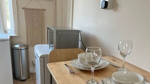 A dining table set with plates, cutlery, and wine glasses, with a trash bin and a small refrigerator in the background. - Flat 1,1 bedroom flat sleeps 4 in Abingdon Oxfordshire (Abingdon)