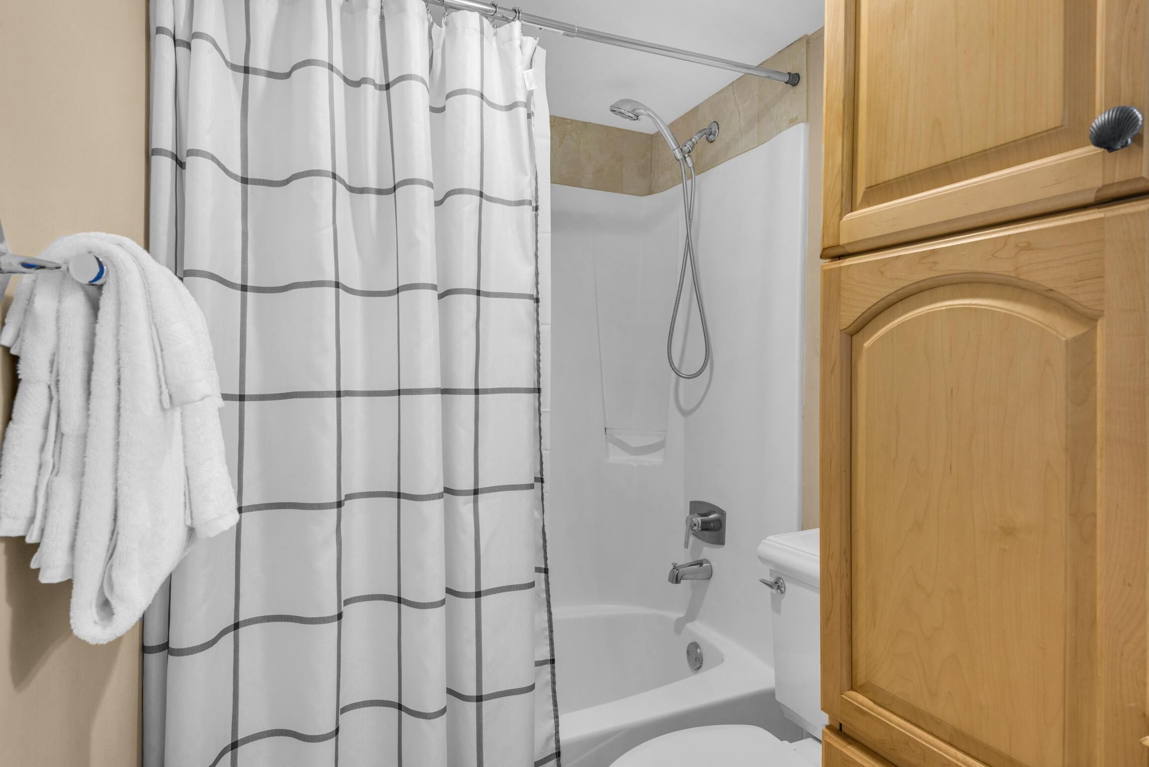 A bathroom with a shower, a toilet, and a wooden cabinet.