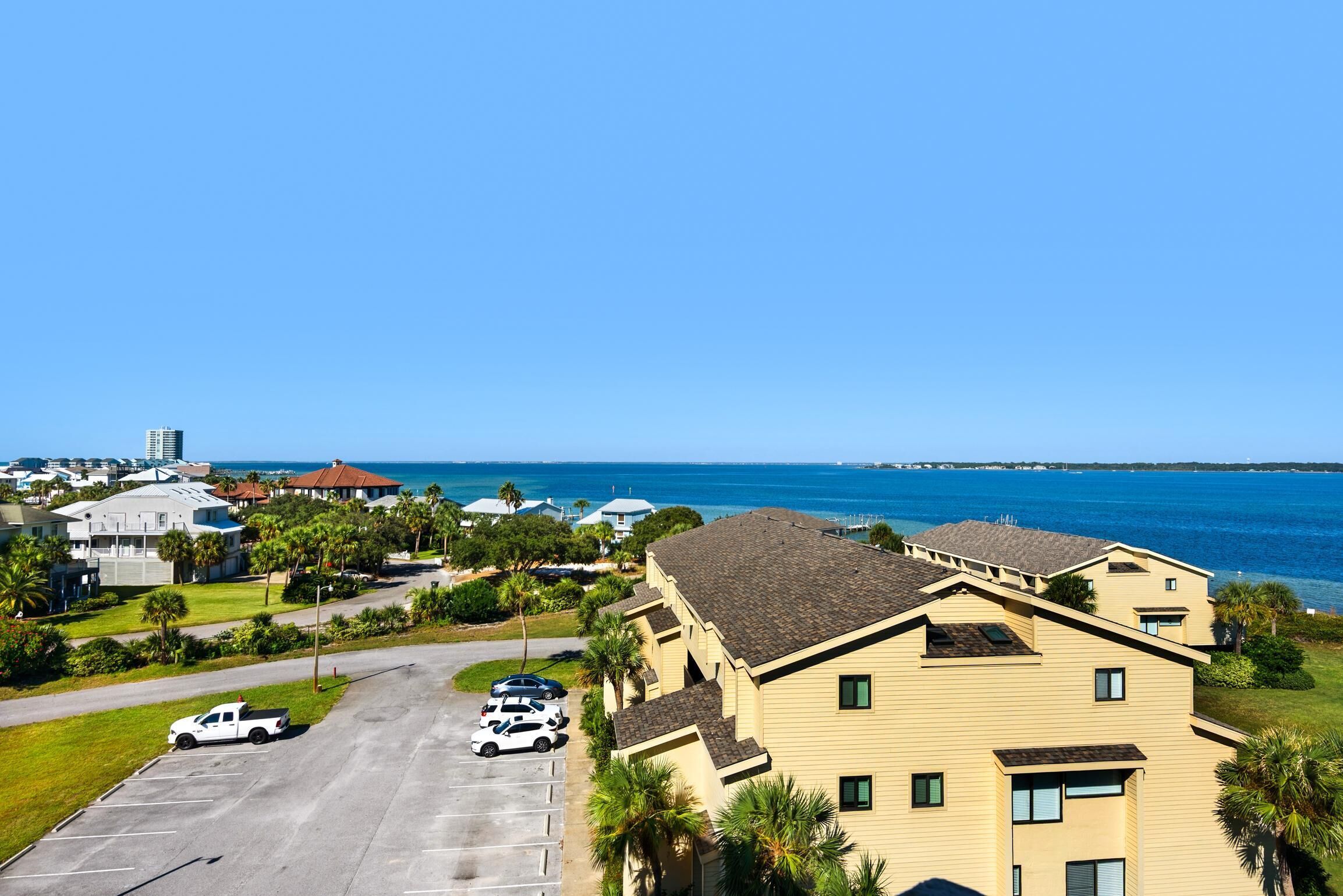 A coastal hotel with a parking lot, several cars, and a view of the ocean.