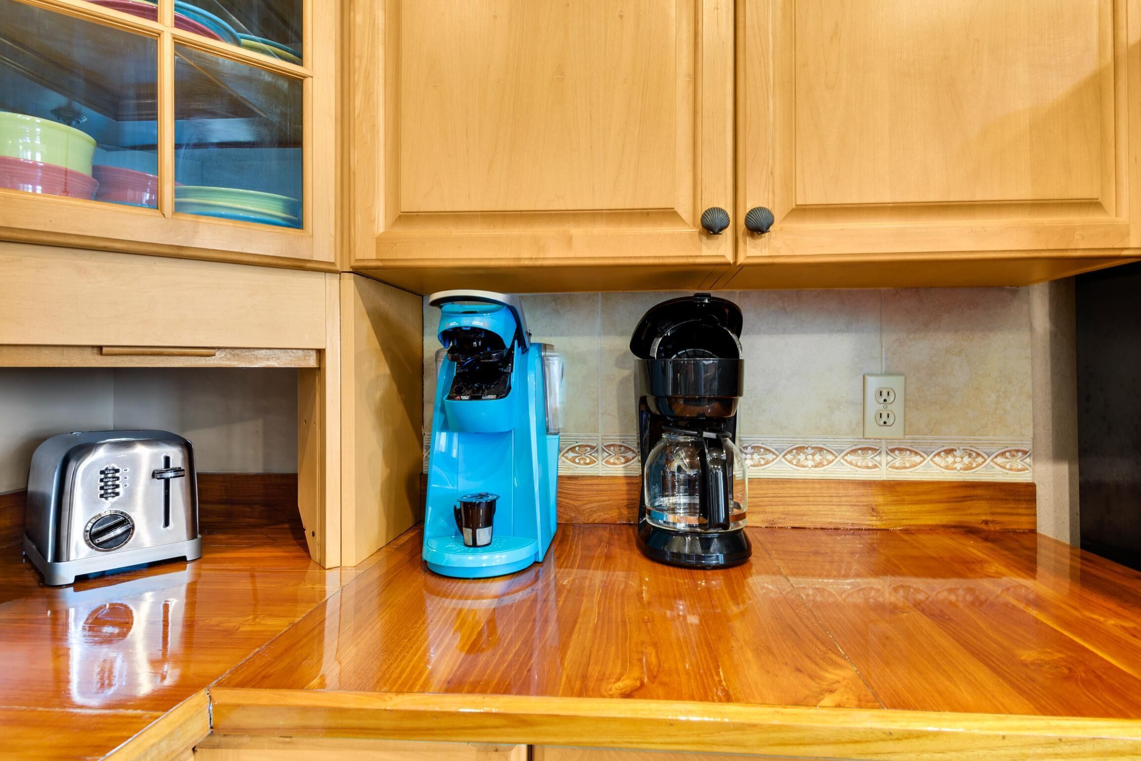 A kitchen with wooden cabinets, a toaster, a blue coffee maker, and a black coffee maker on a wooden countertop.