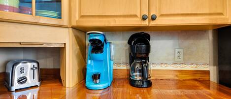 A kitchen with wooden cabinets, a toaster, a blue coffee maker, and a black coffee maker on a wooden countertop.