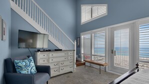 A bedroom with a bed, a TV, a dresser, a bench, and a staircase. - White Sands 451- Beach Dreams (Pensacola Beach)