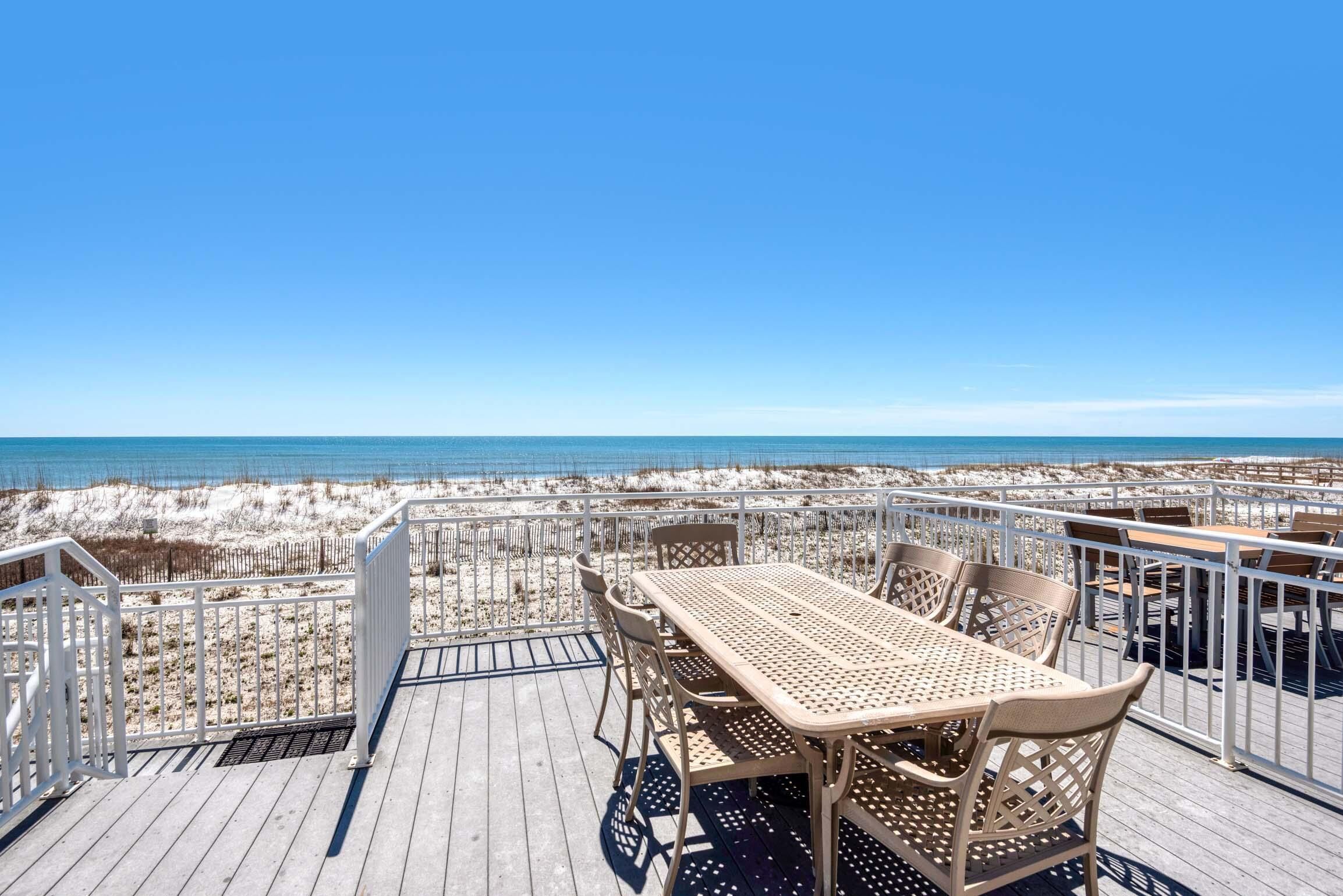 A deck with a table and chairs overlooking a beach.