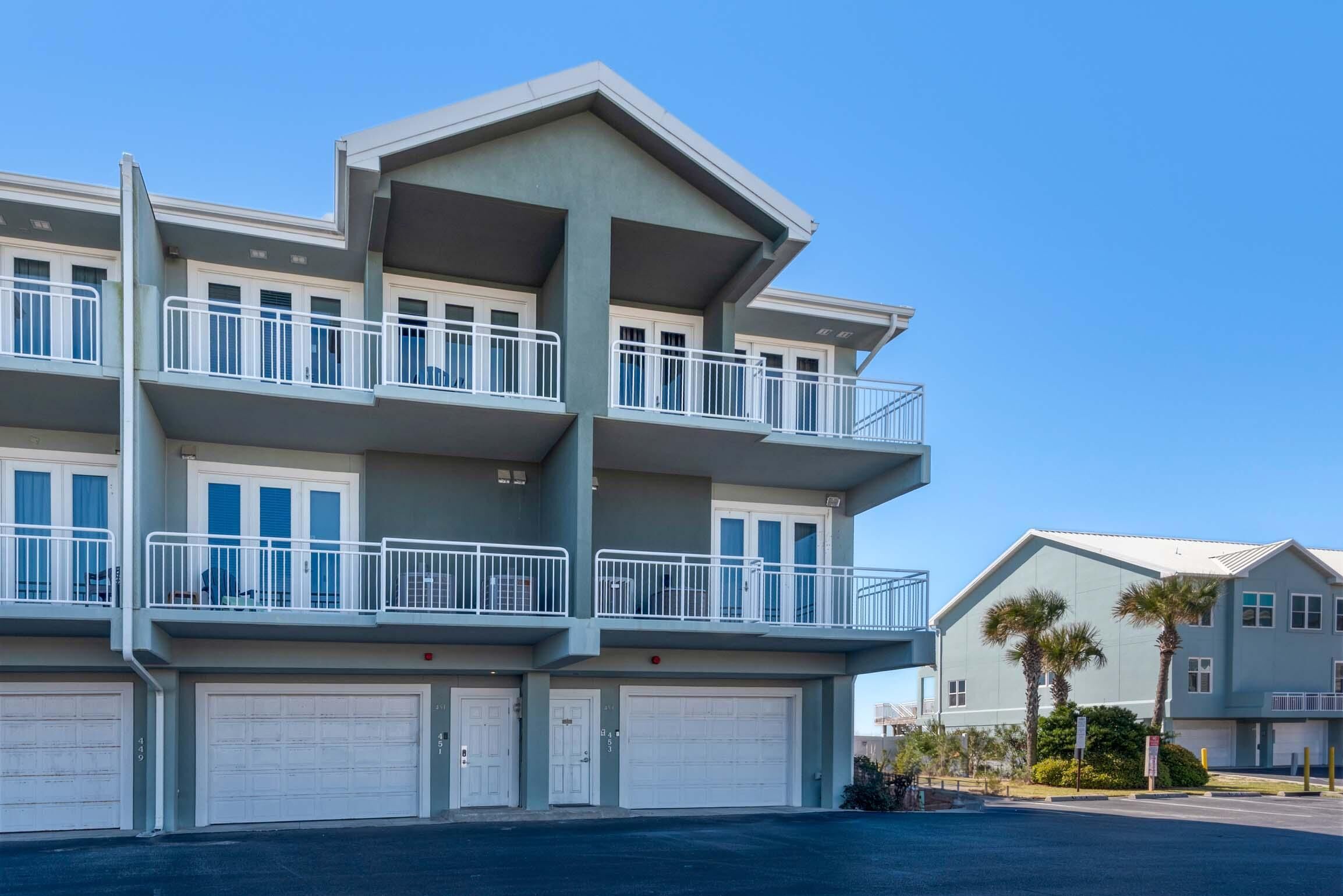 A multi-story residential building with balconies, garage doors, and a clear blue sky.